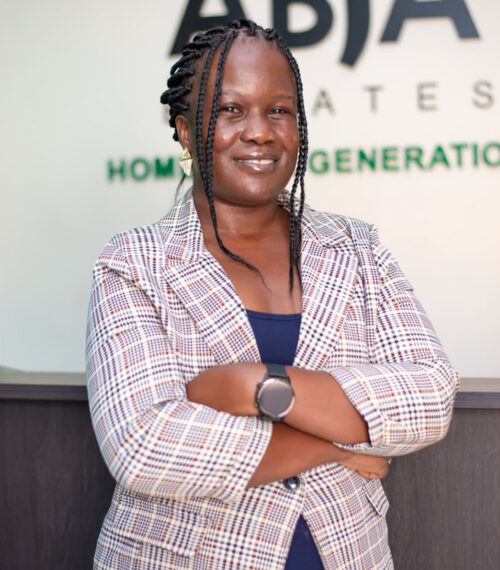 Portrait of female founder sitting at a conference table with laptop, late 30s, professional blazer, warm expression while holding a coffee cup